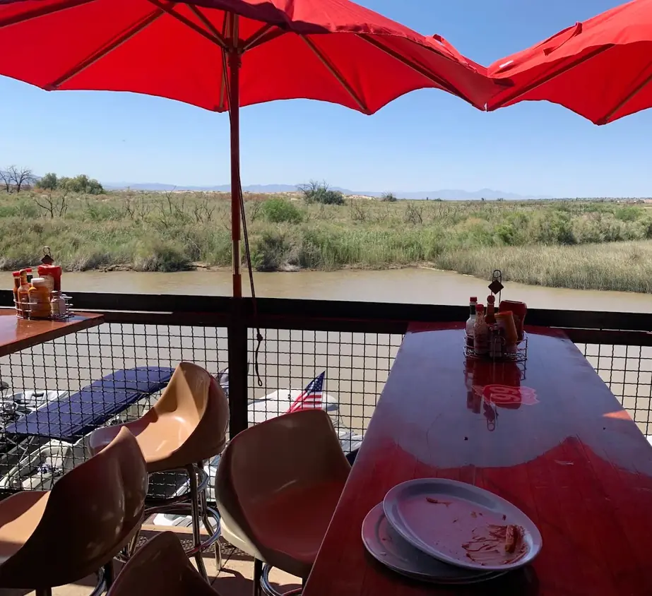 A table on the Topock66 river deck under red umbrellas, the reeds and the river beyond the rail
