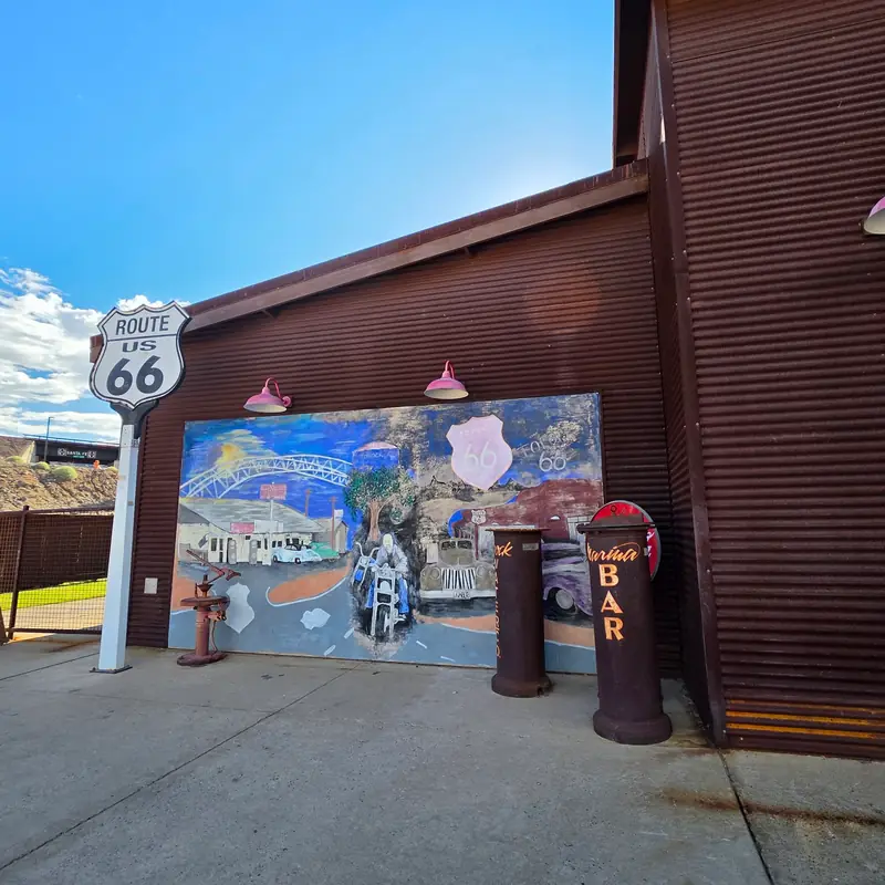 The US 66 shield sign beside the painted Route 66 mural and the Marina Bar barrels